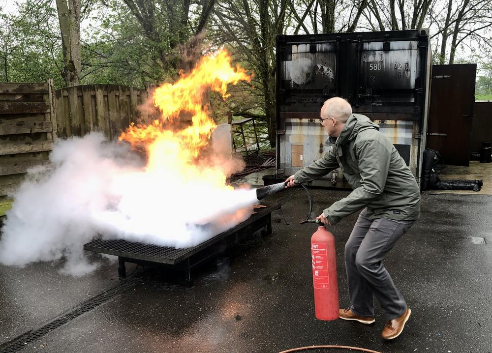 Deelnemer van een BHV training van LuxBHV blust een vloeistofbrand met een poederblusser op het oefenterrein